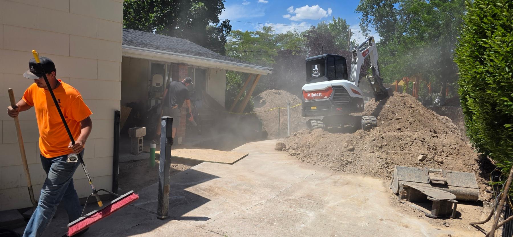 A J&J crew member sweeping the drive while an excavator digs behind him