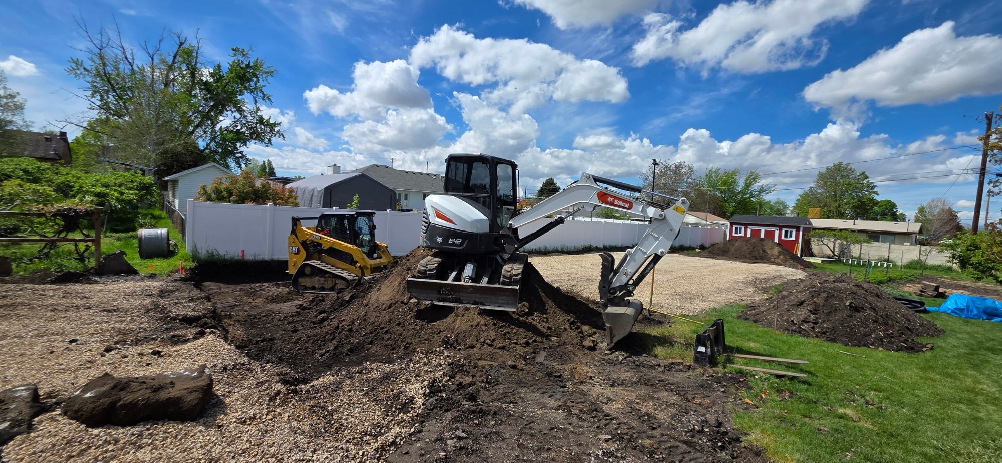 An excavator and a track loader working open ground on a residential site