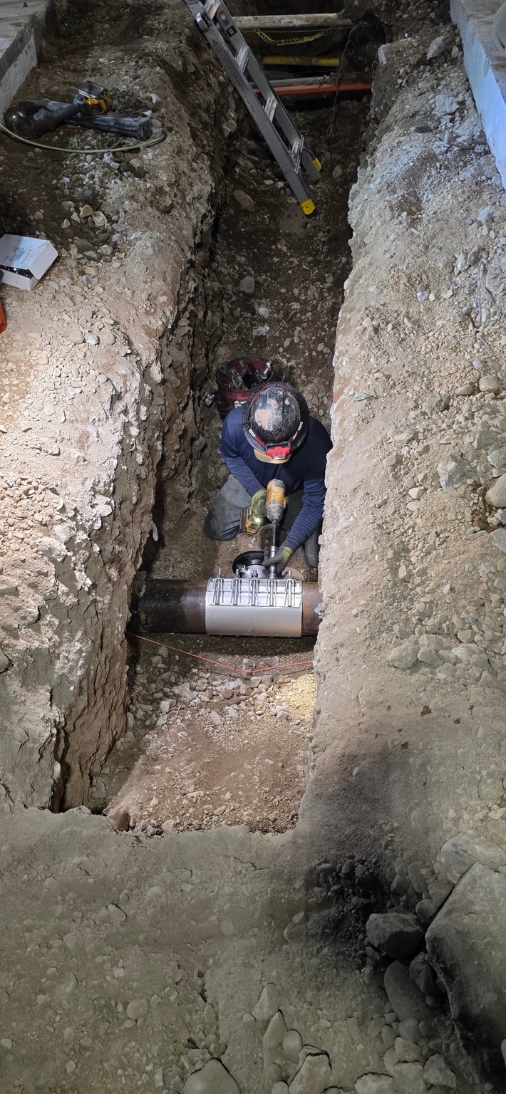 A J&J crew member down in a trench making a connection to a live water main