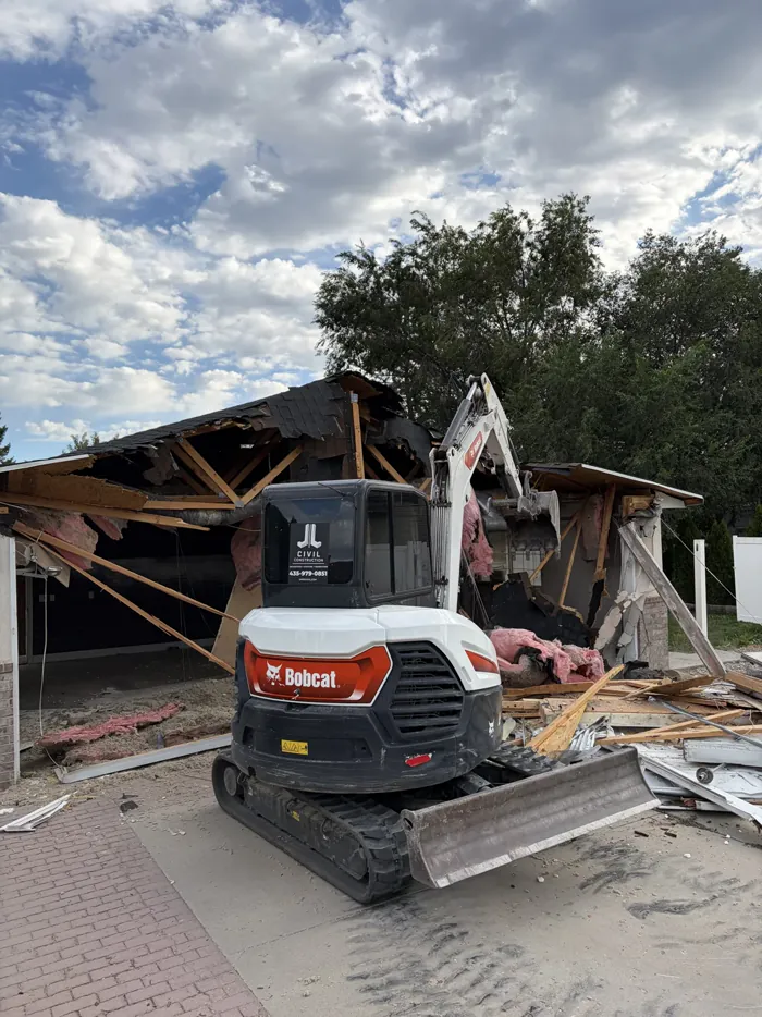 An excavator pulling apart a carport structure during a residential demolition