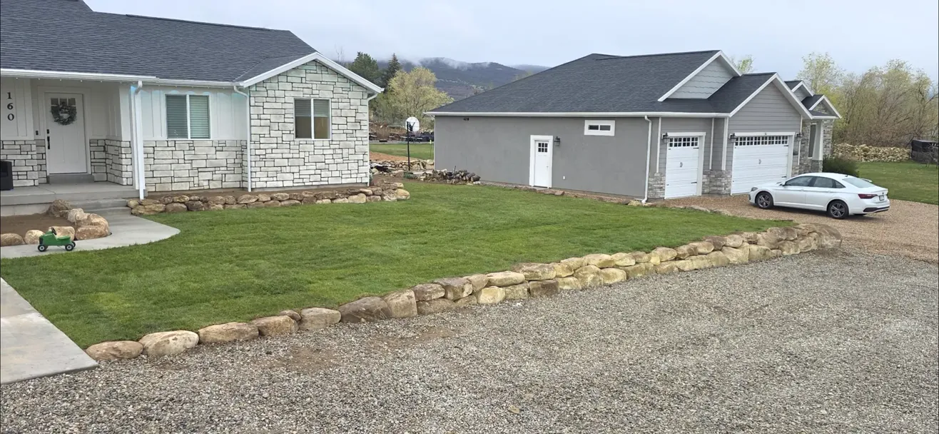 A finished front yard with new lawn, boulder edging and a gravel driveway