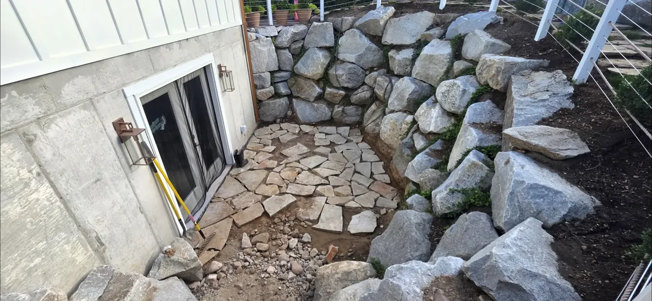 A boulder retaining wall built out against a house with a stone landing below