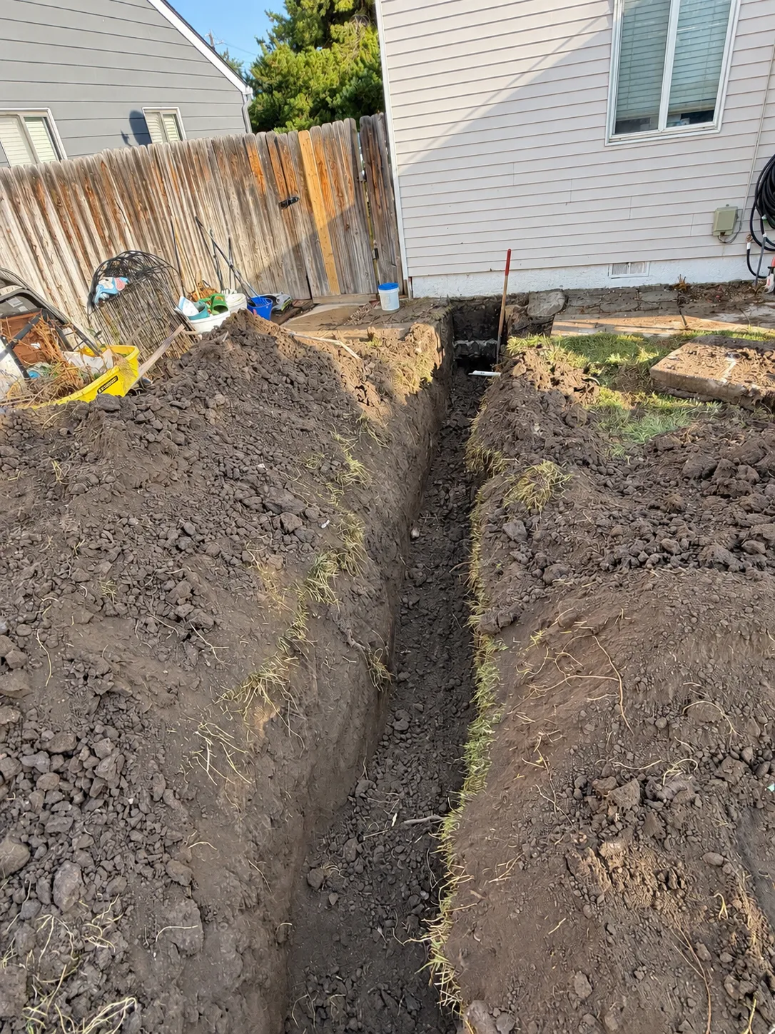 A deep utility trench cut with clean vertical walls beside an existing house